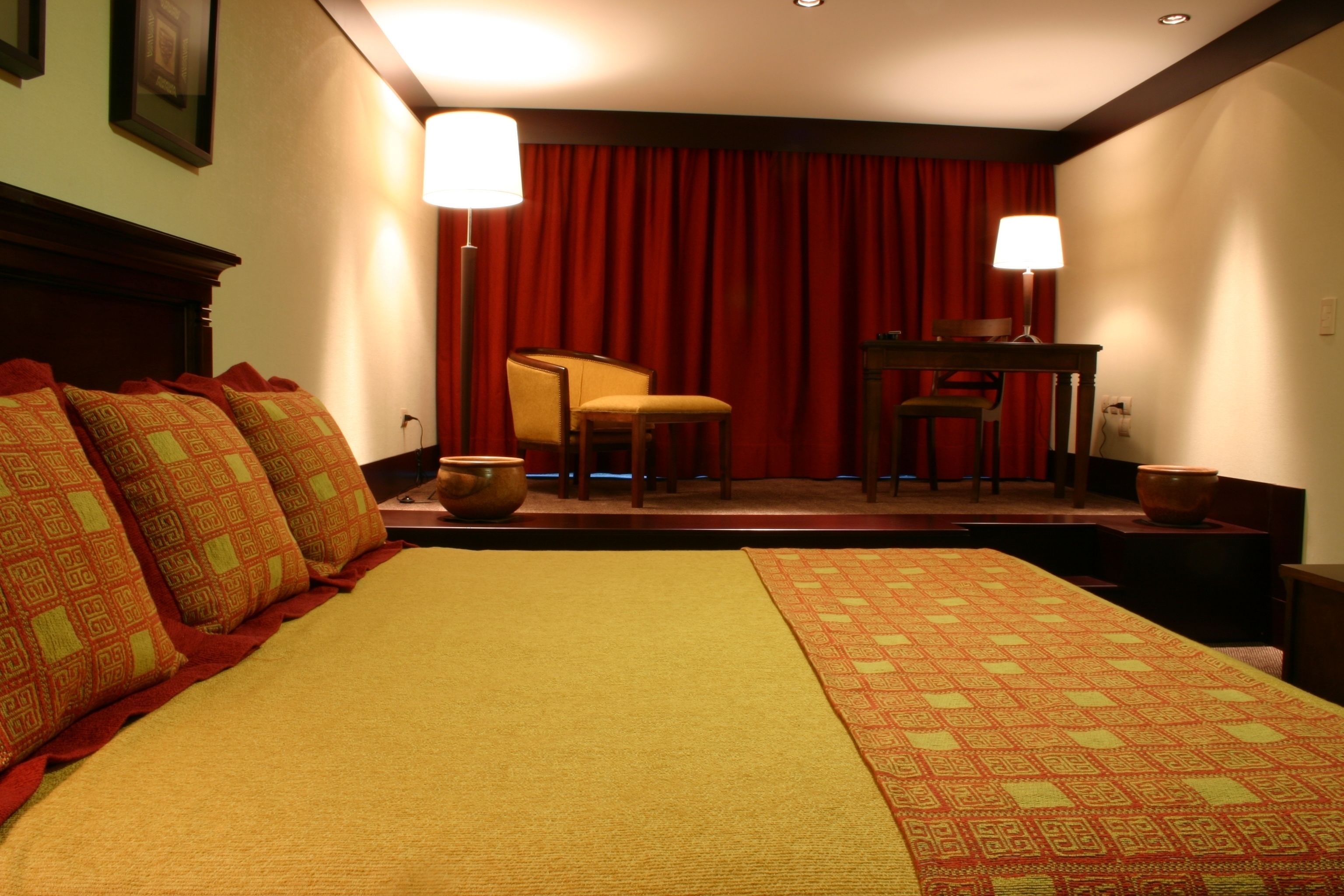 Une chambre d’hôtel avec un grand lit, deux chaises, un bureau et un rideau rouge en arrière-plan.