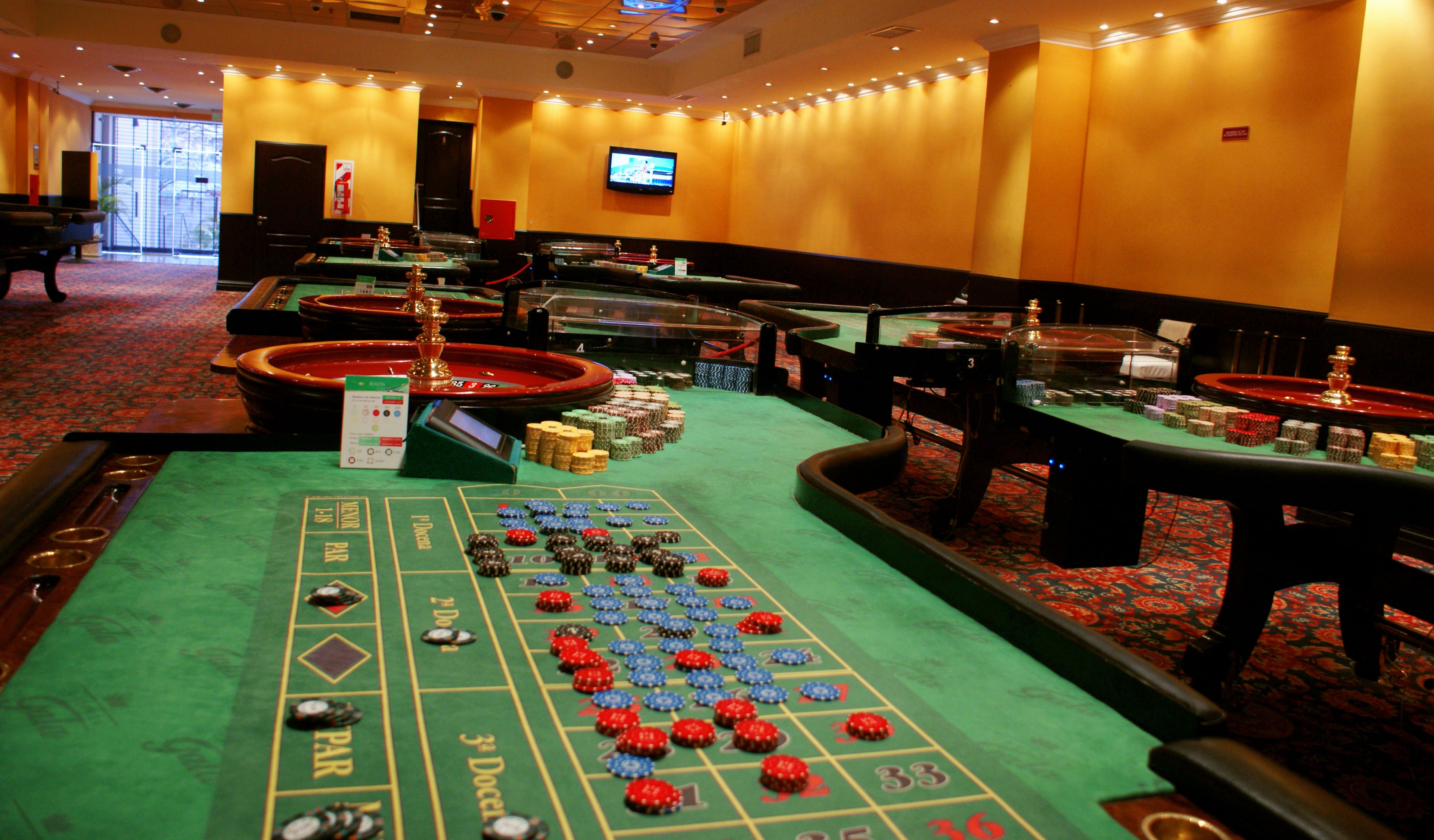 A casino floor with multiple blackjack tables, roulette wheels, and a craps table.