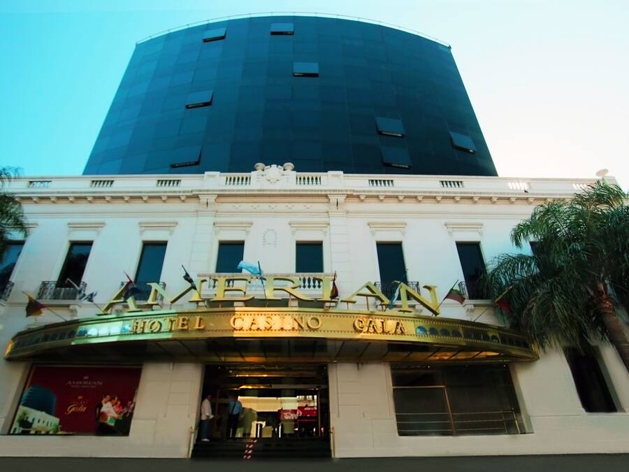 The exterior of the Amerian Hotel Casino & Spa, featuring a prominent curved marquee with the hotel's name, a large glass atrium, and classical architectural details.