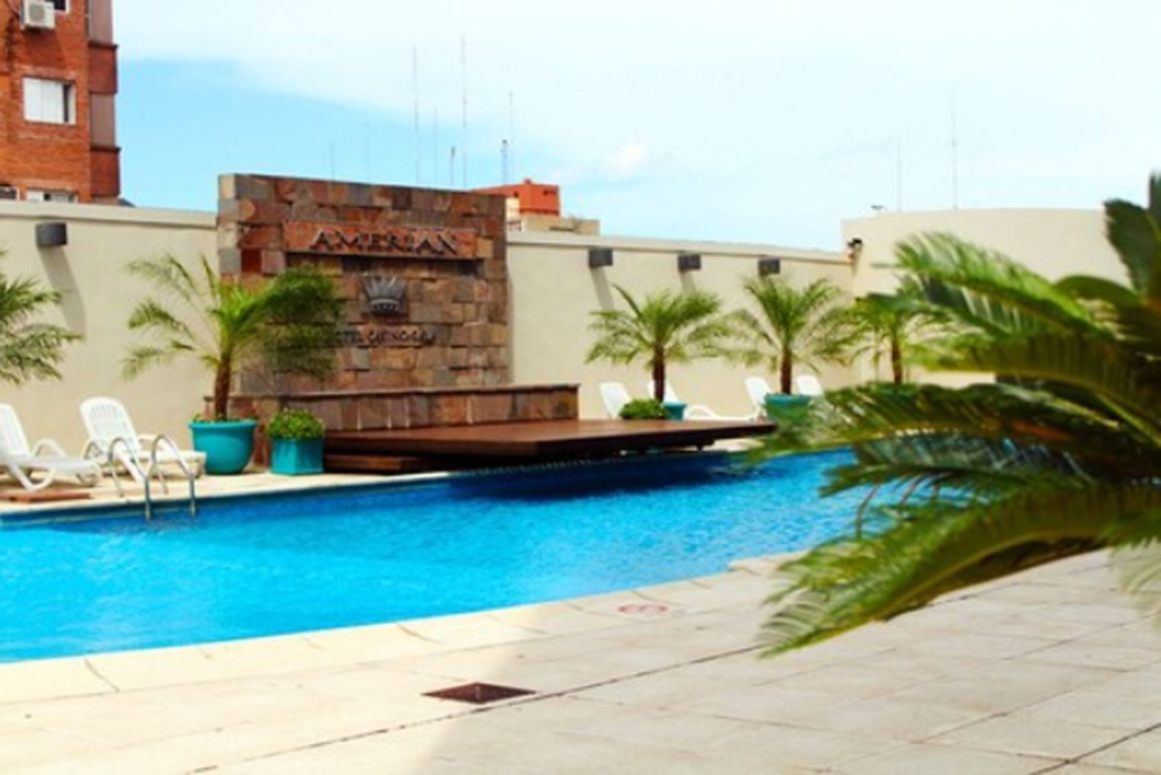 Una piscina con sillas de descanso, palmeras y un muro de piedra con la palabra "AMERICAN".