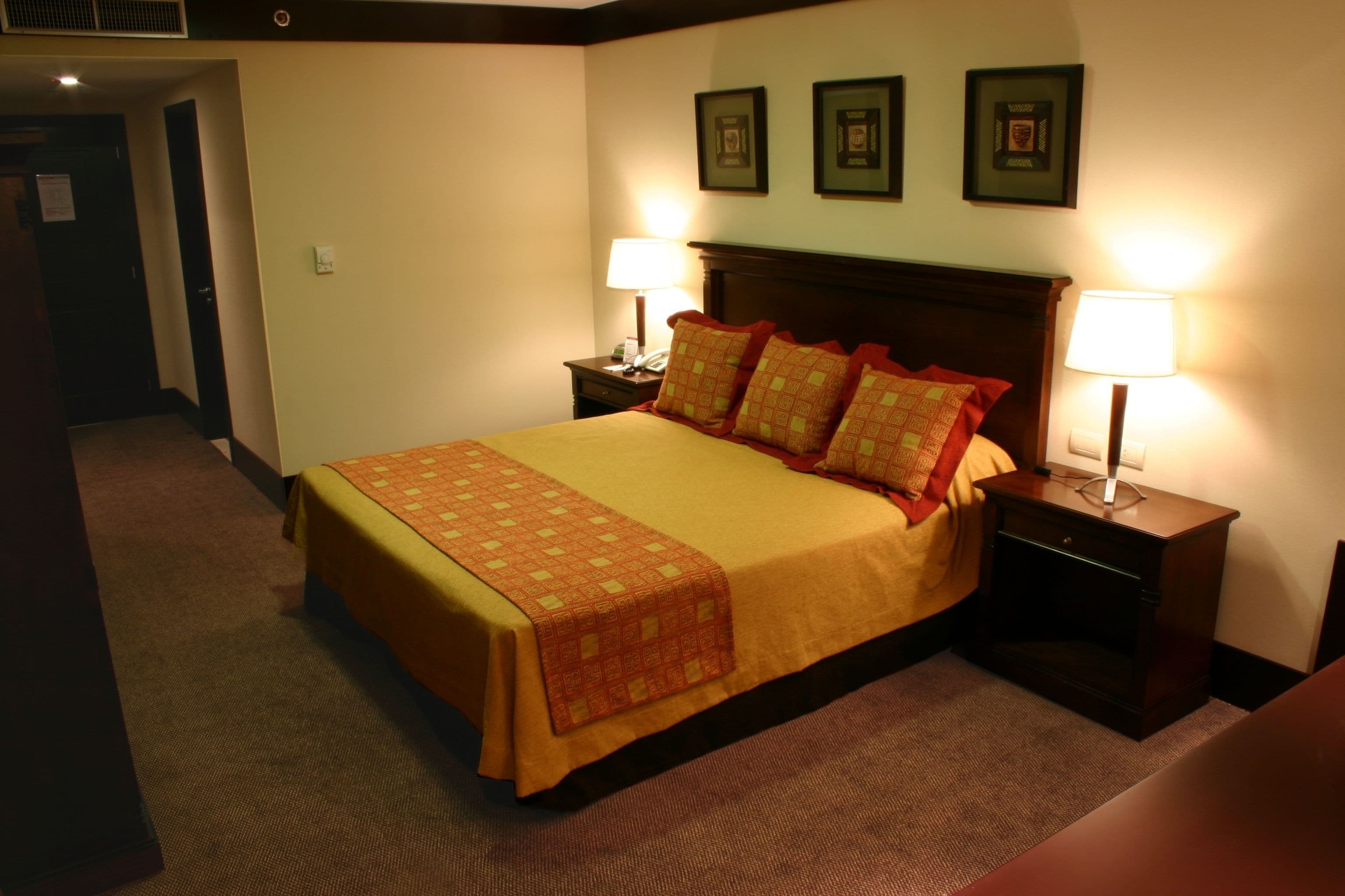 Una habitación de hotel con una cama grande, dos mesitas de noche con lámparas y tres cuadros en la pared.