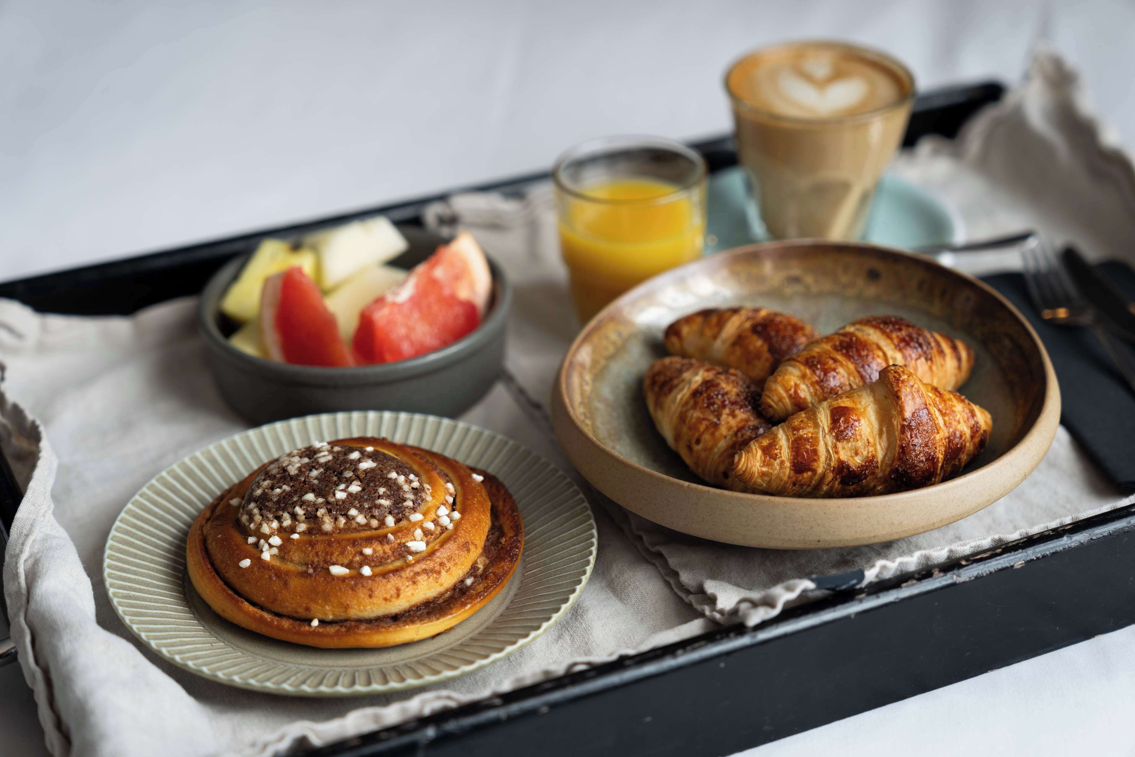A breakfast tray with croissants, a cinnamon roll, and a bowl of fruit.
