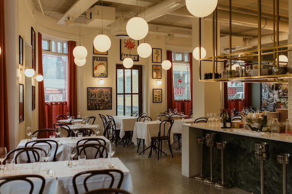 A restaurant interior with tables, chairs, hanging lights, and a bar area.