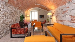 A cozy living room with brick walls, orange sofas, and a large window providing natural light. - Hotel an der Aare Swiss Quality (Solothurn)