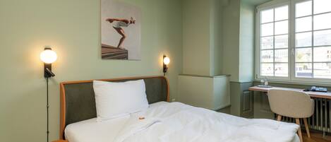 A hotel room with a bed, a desk, a chair, and a window.