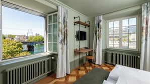 A room with a bed, a desk with a chair, a TV, and large windows with curtains. - Hotel an der Aare Swiss Quality (Solothurn)