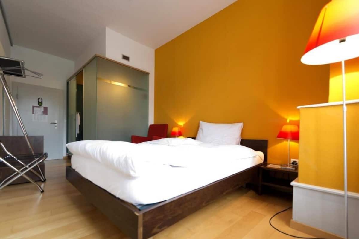 A hotel room with a bed, two bedside lamps, a chair, and a desk.