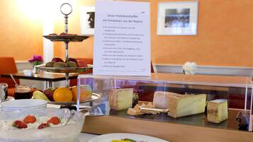 A buffet with various food items including fruits, cheeses, and a dessert.