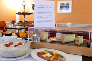 Un bufé con diferentes opciones de comida, entre ellas frutas, quesos y un postre.