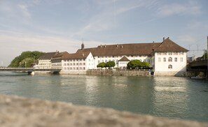 Un edificio histórico con un río frente a él, que presenta un puente y un muro de piedra.