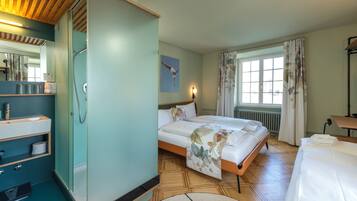 Ein Hotelzimmer mit Bett, Bad mit Dusche, Waschbecken und einem Fenster mit Vorhängen.