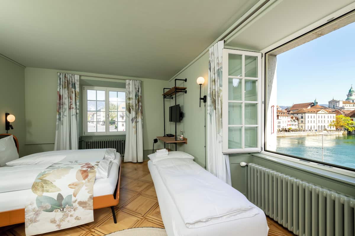 A hotel room with two beds, a view of a river, and a cityscape.