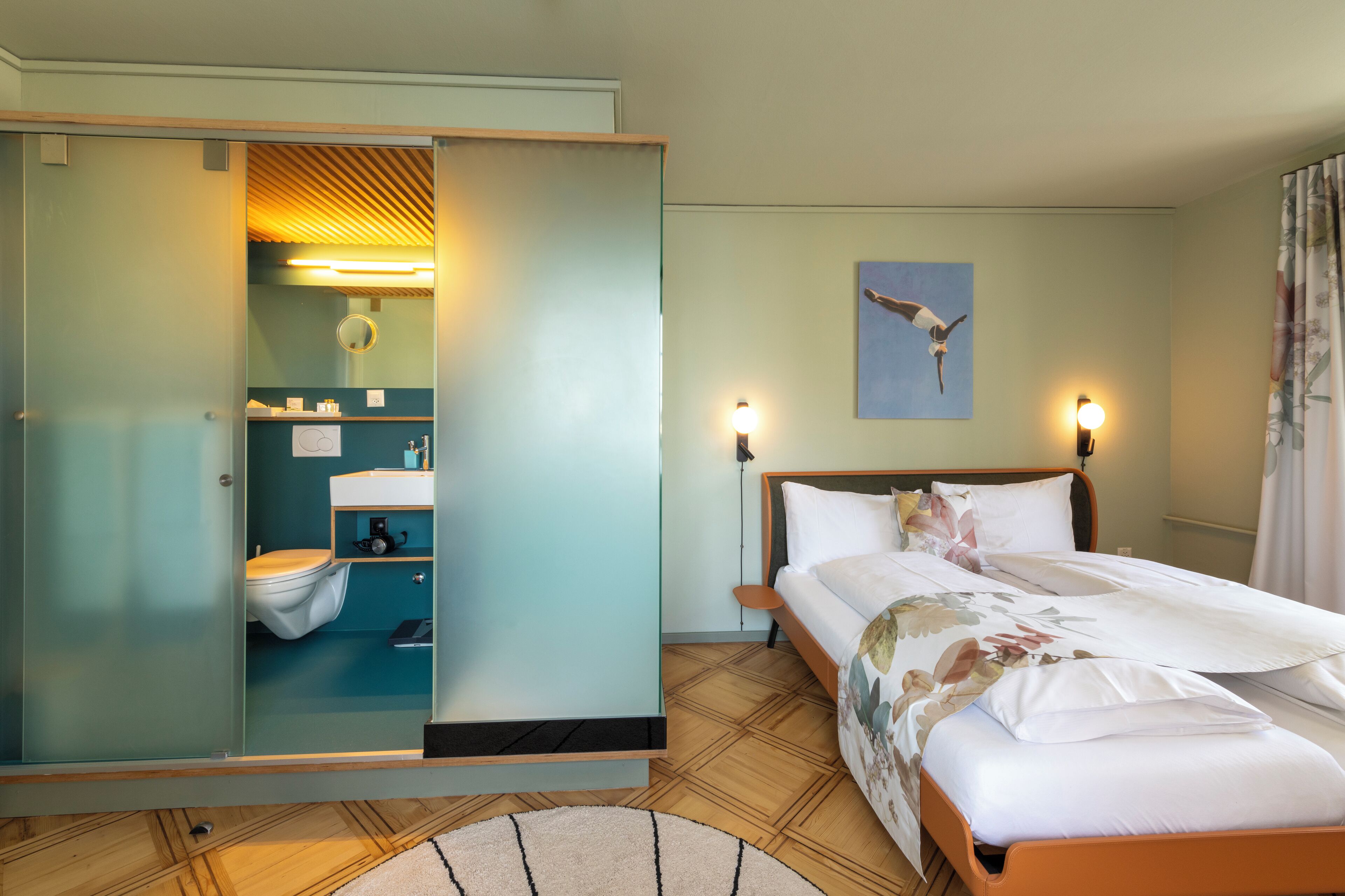 A hotel room with a bed, a bathroom with a toilet, and a mirror.
