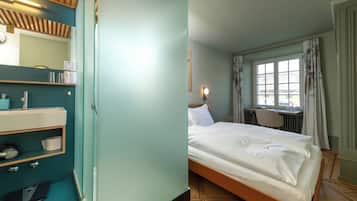 A hotel room with a bed, a desk, a chair, a bathroom with a mirror, and a window with curtains.