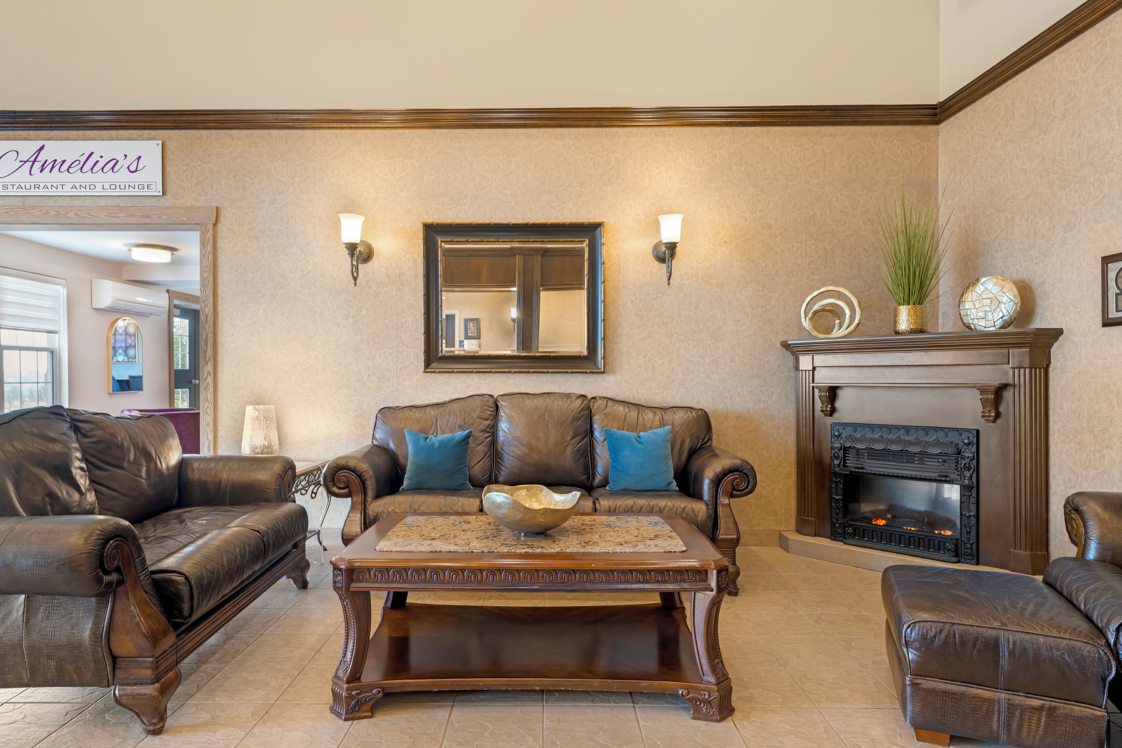A living room with leather sofas, a coffee table, a fireplace, and wall-mounted sconces.