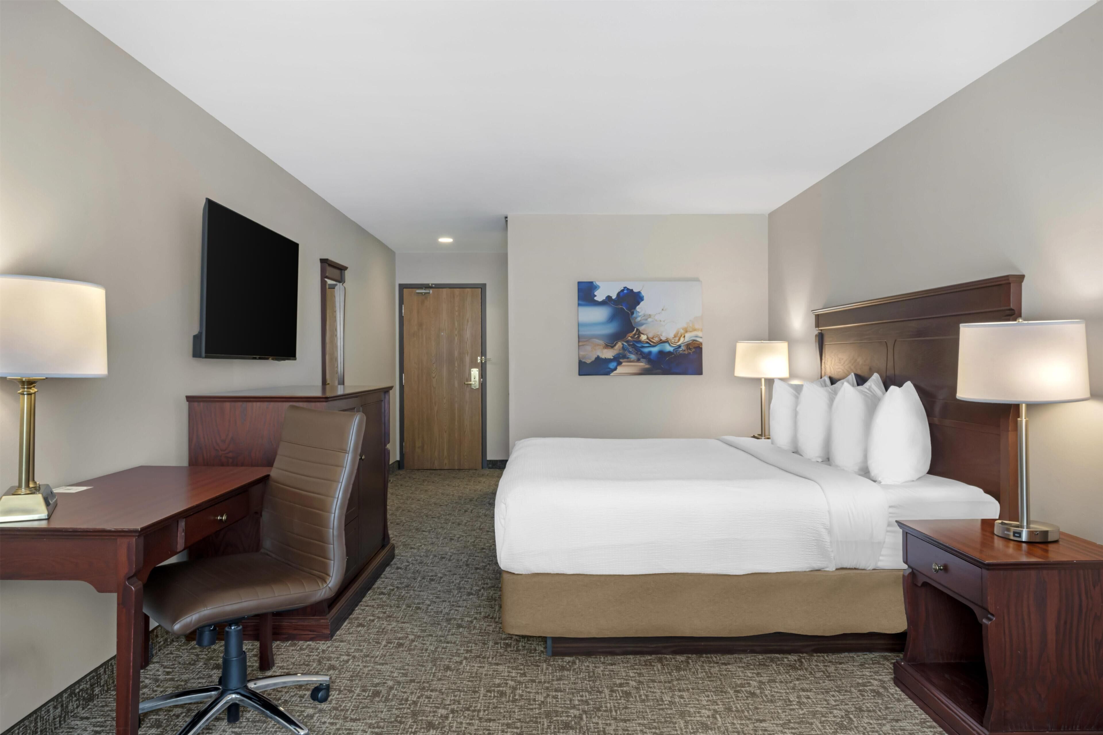 A hotel room with a bed, desk, chair, and a flat-screen TV.