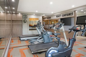 Une salle de sport équipée de tapis de course, de vélos d’appartement et d’une horloge murale.