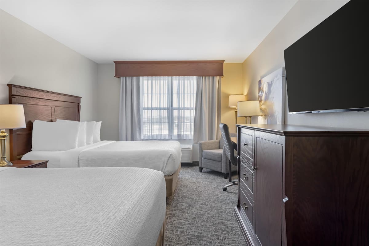 A hotel room with two beds, a desk, a chair, a television, and a window with curtains.