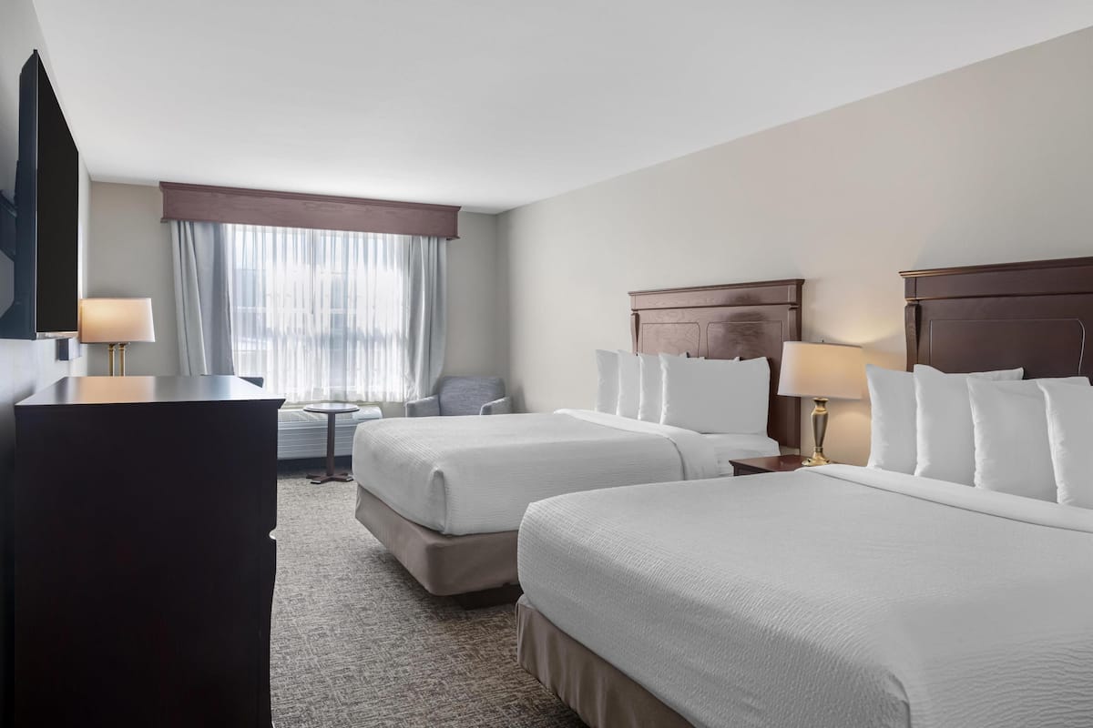 A hotel room with two beds, a desk, a chair, a TV, and a window with curtains.