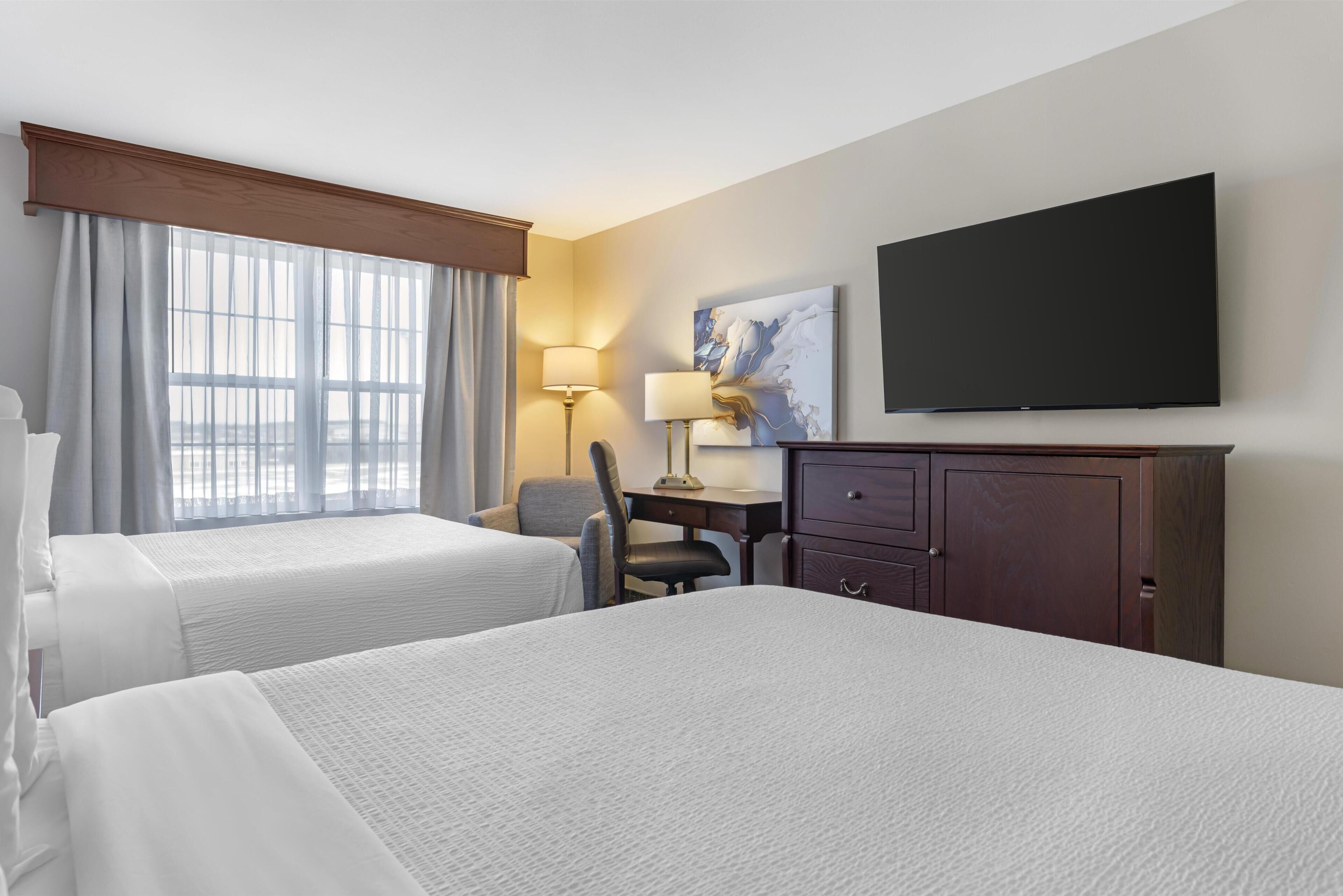 A hotel room with two beds, a desk, a chair, a TV, and a painting on the wall.