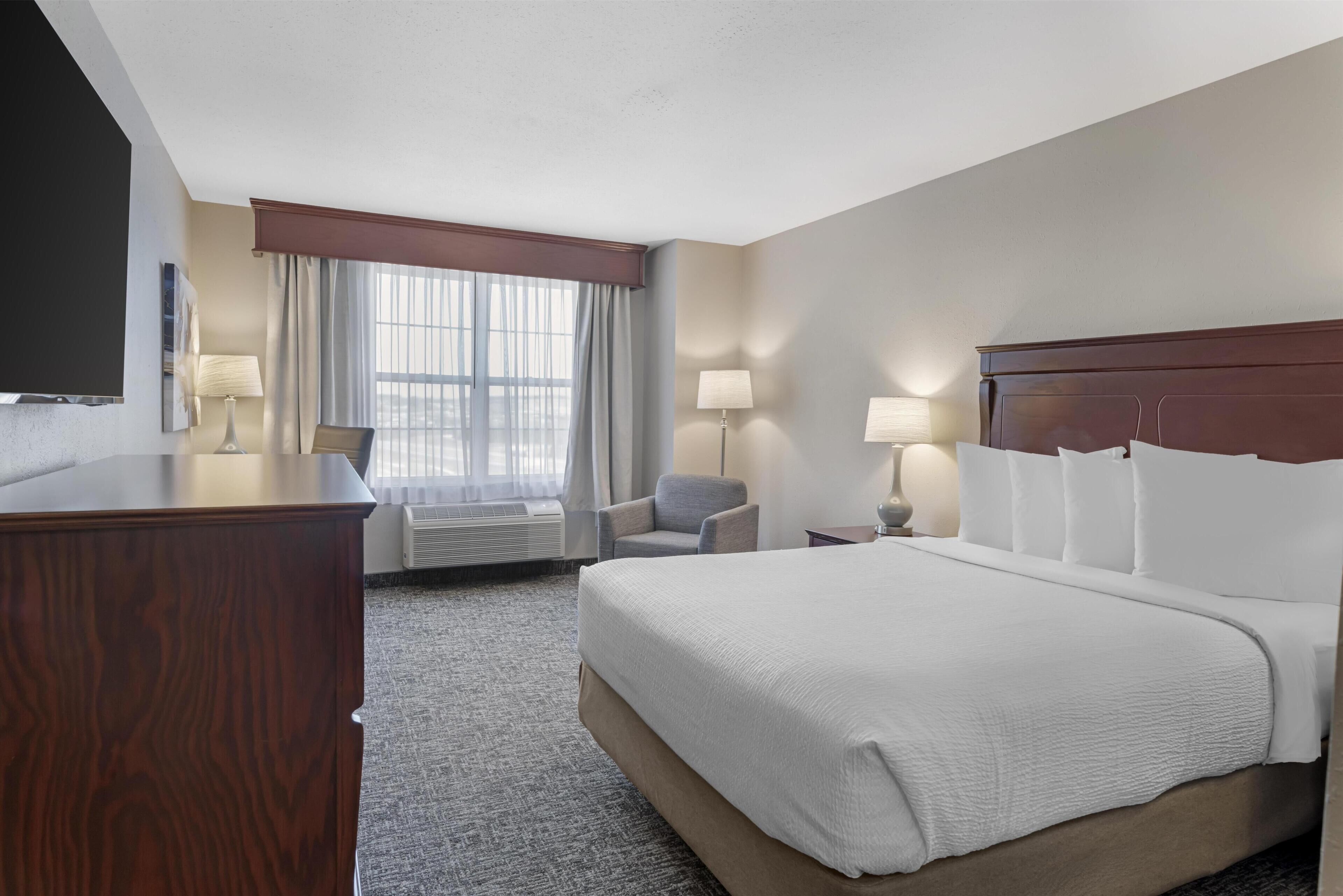 Habitación de hotel con una cama grande, un escritorio, una silla, un televisor y una ventana con cortinas.