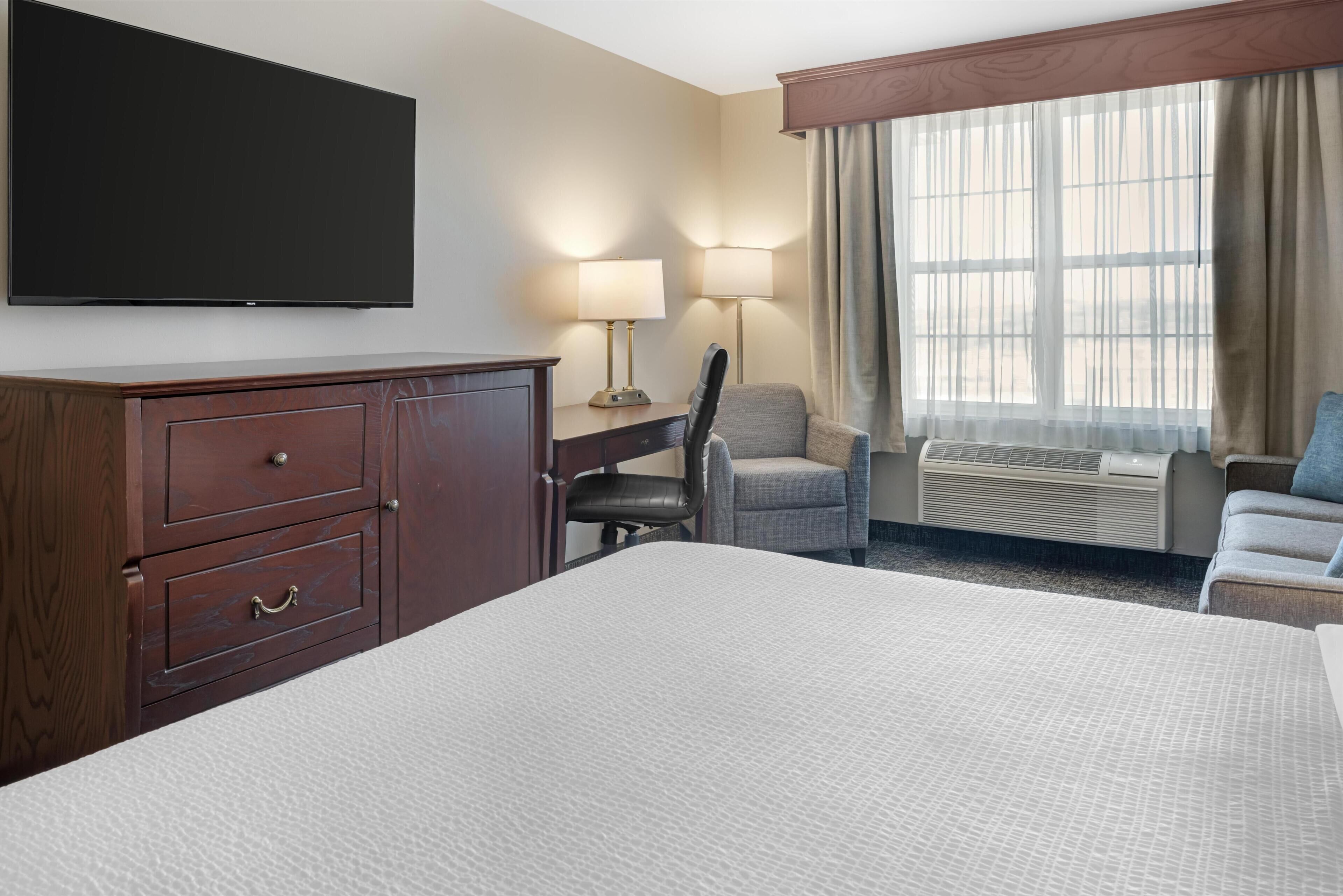 Een hotelkamer met een bed, een bureau, een stoel, een televisie en een raam met gordijnen.