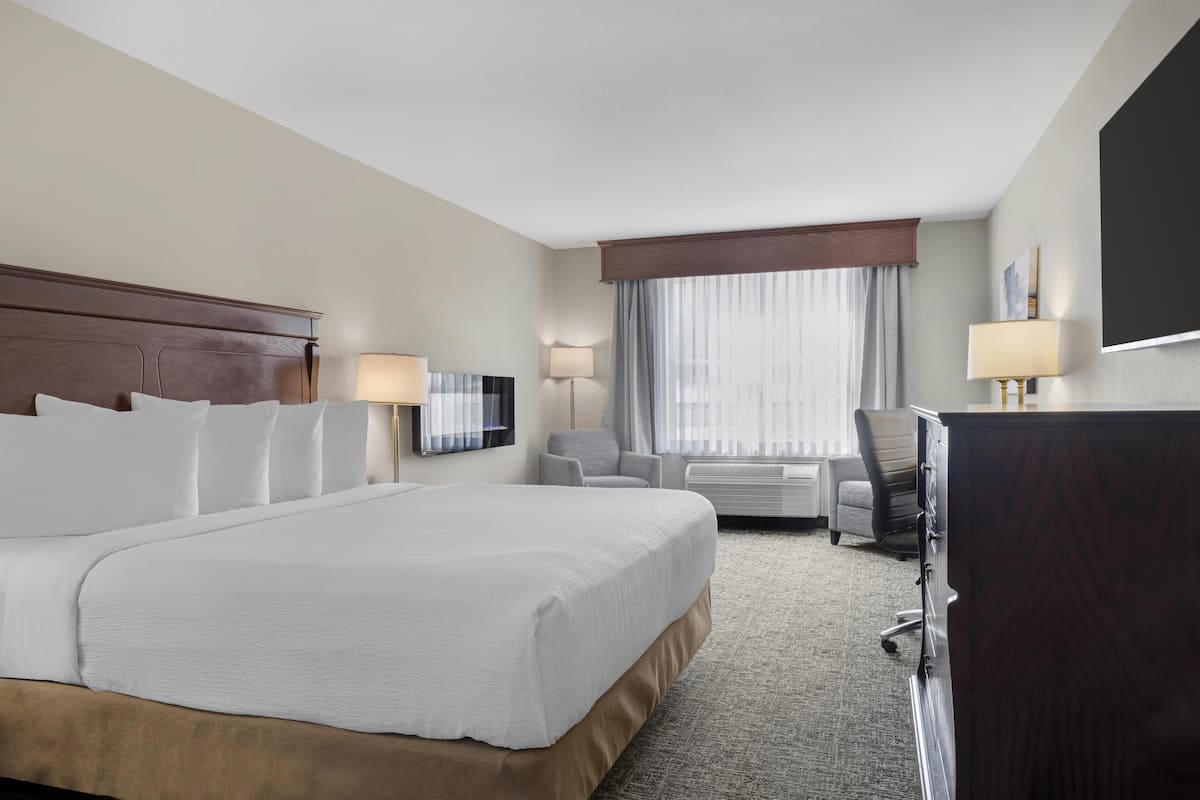 A hotel room with a large bed, a desk, a chair, a television, and a window with curtains.