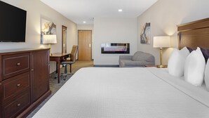Een hotelkamer met een groot bed, een bureau, een stoel, een televisie en een open haard.