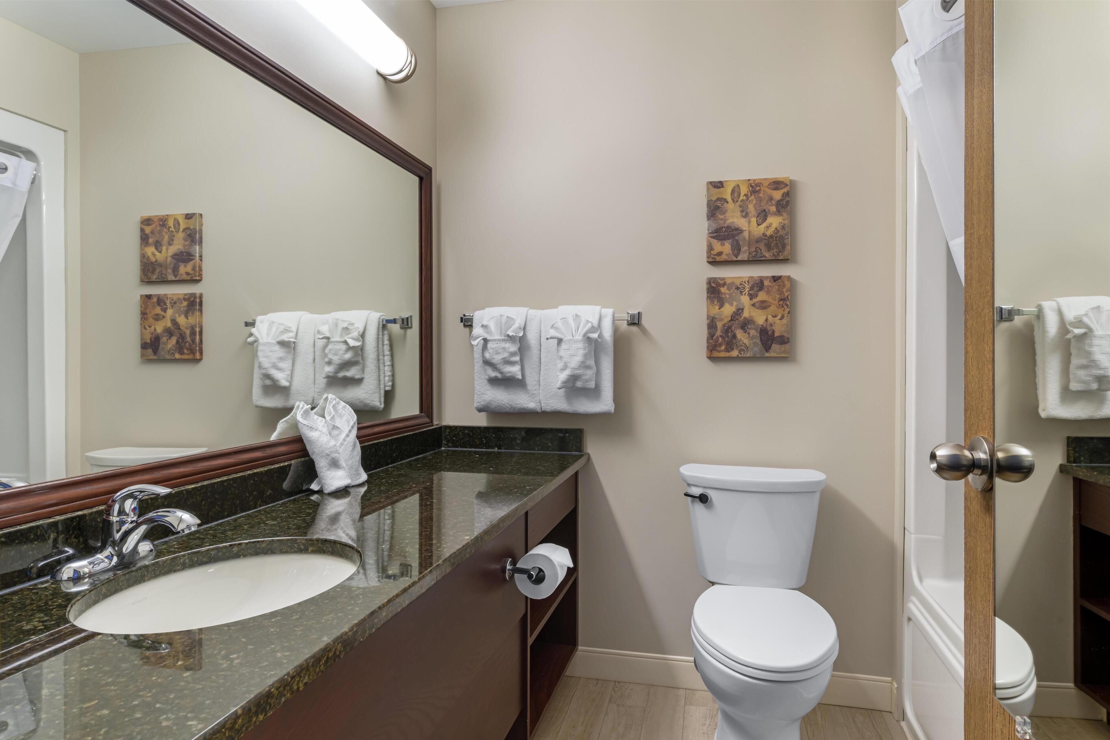 A bathroom with a sink, mirror, toilet, and towels.