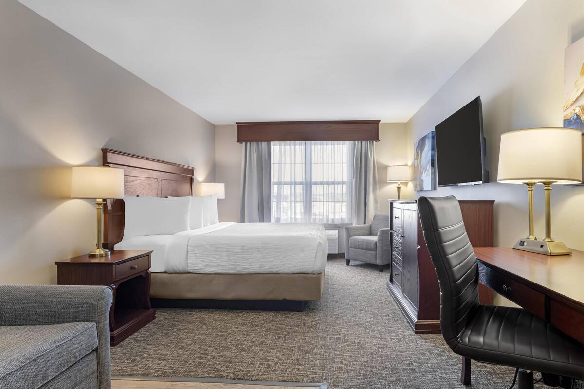A hotel room with a bed, a desk, a chair, a television, and a window with curtains.