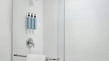A glass-enclosed shower with a handheld showerhead, a towel rack, and a set of toiletries on the wall.