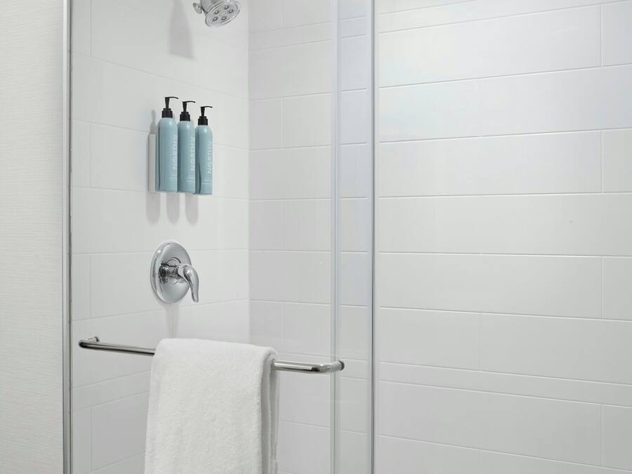 A glass-enclosed shower with a handheld showerhead, a towel rack, and a set of toiletries on the wall.