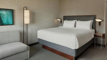 A hotel room with a bed, a chair, a lamp, and a painting on the wall.