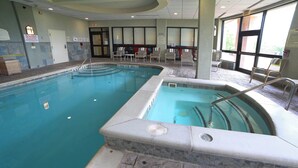 Una piscina interior con agua cristalina, un borde de baldosas y una zona de estar con sillas.