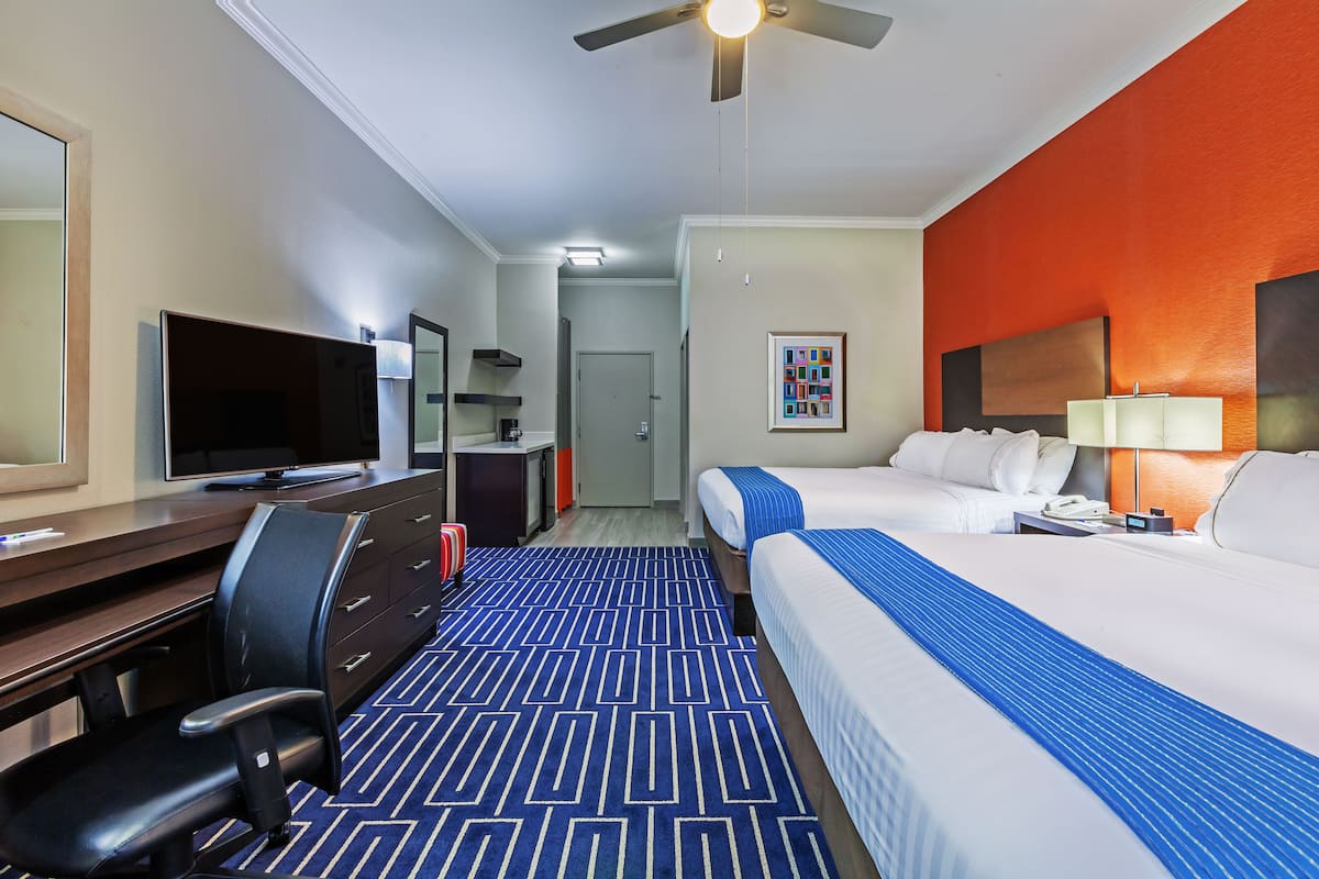 A hotel room with a bed, desk, chair, television, and a ceiling fan.