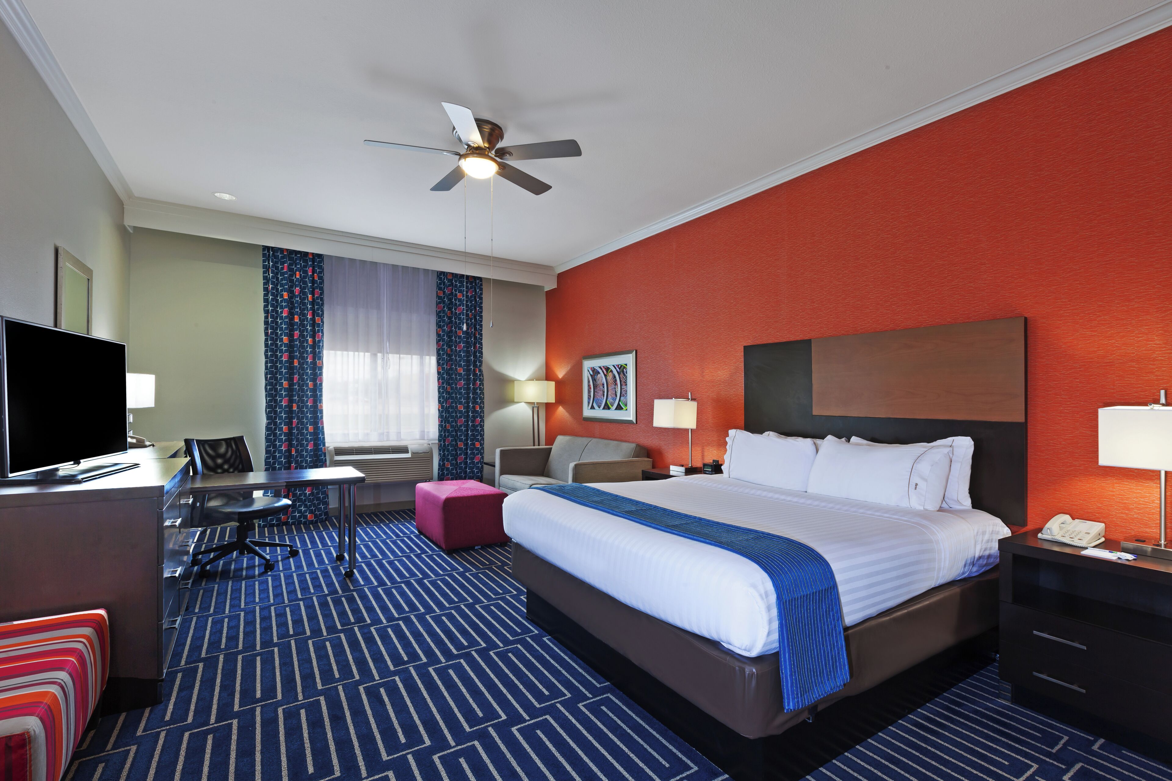 A hotel room with a bed, desk, chair, television, and a ceiling fan.