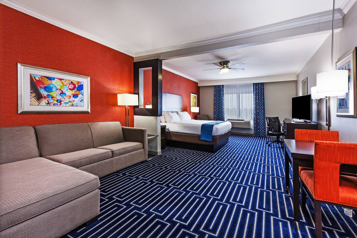 A hotel room with a large bed, a sofa, a desk, and a television.