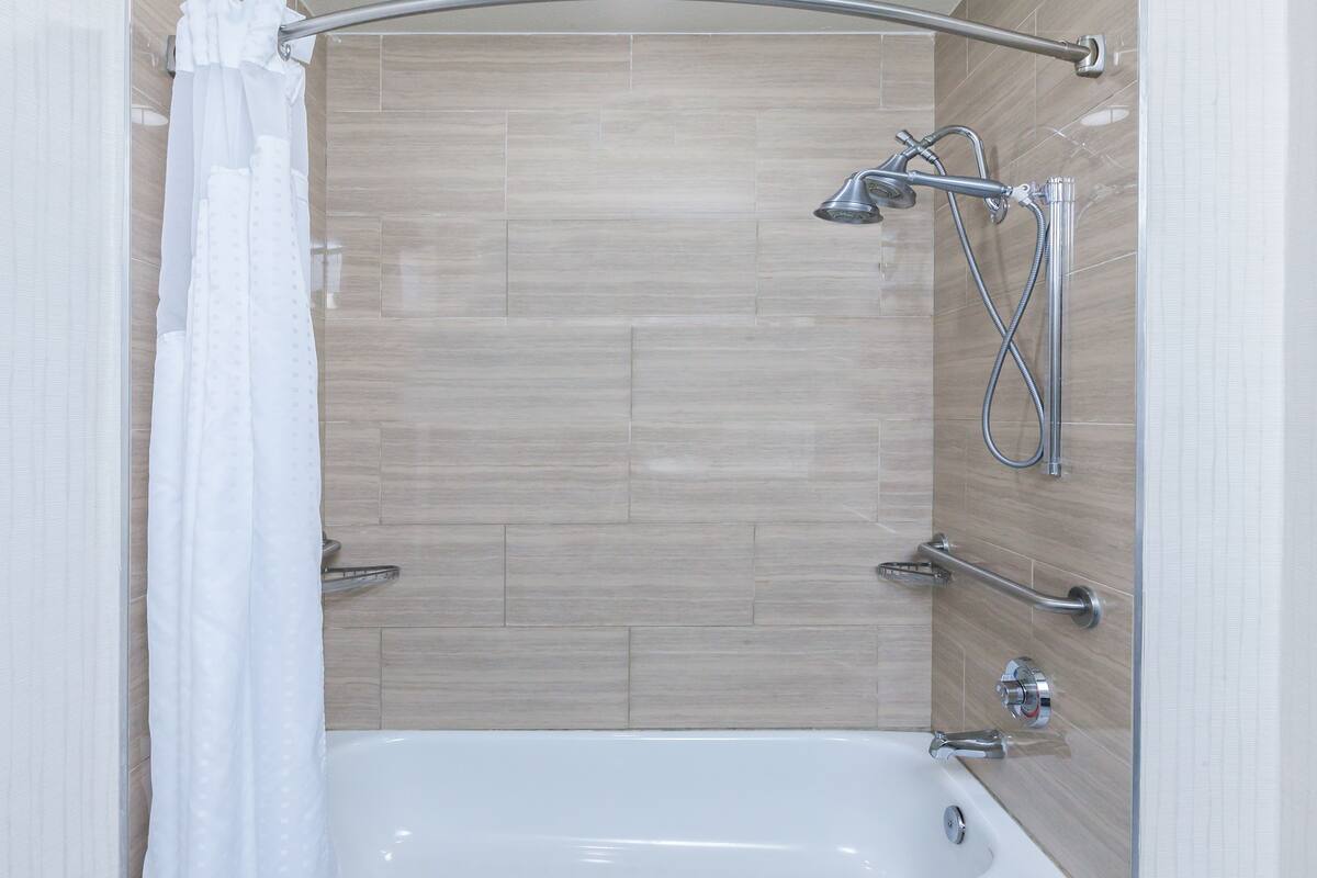 A modern bathroom with a bathtub, shower, and handrails.