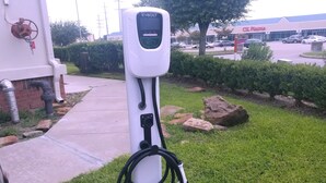 A public EV charging station with a digital display, located in a grassy area with a paved path nearby. - Holiday Inn Express & Suites Houston East, by IHG (Houston)