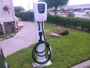 Eine öffentliche Ladestation für Elektrofahrzeuge mit digitalem Bildschirm, gelegen in einer grünen Umgebung mit einem befestigten Weg in der Nähe.