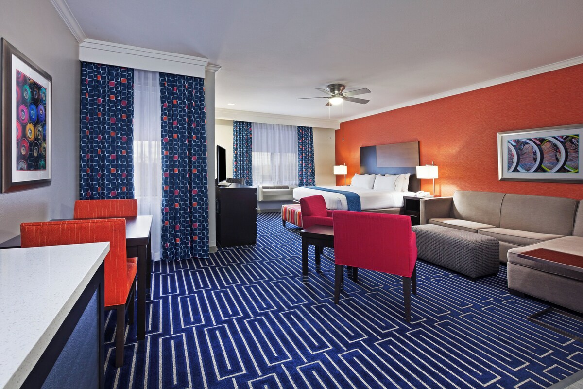 Ein Hotelzimmer mit einem Bett, einem Schreibtisch, einem Sessel, einer Couch und einem Fernseher.