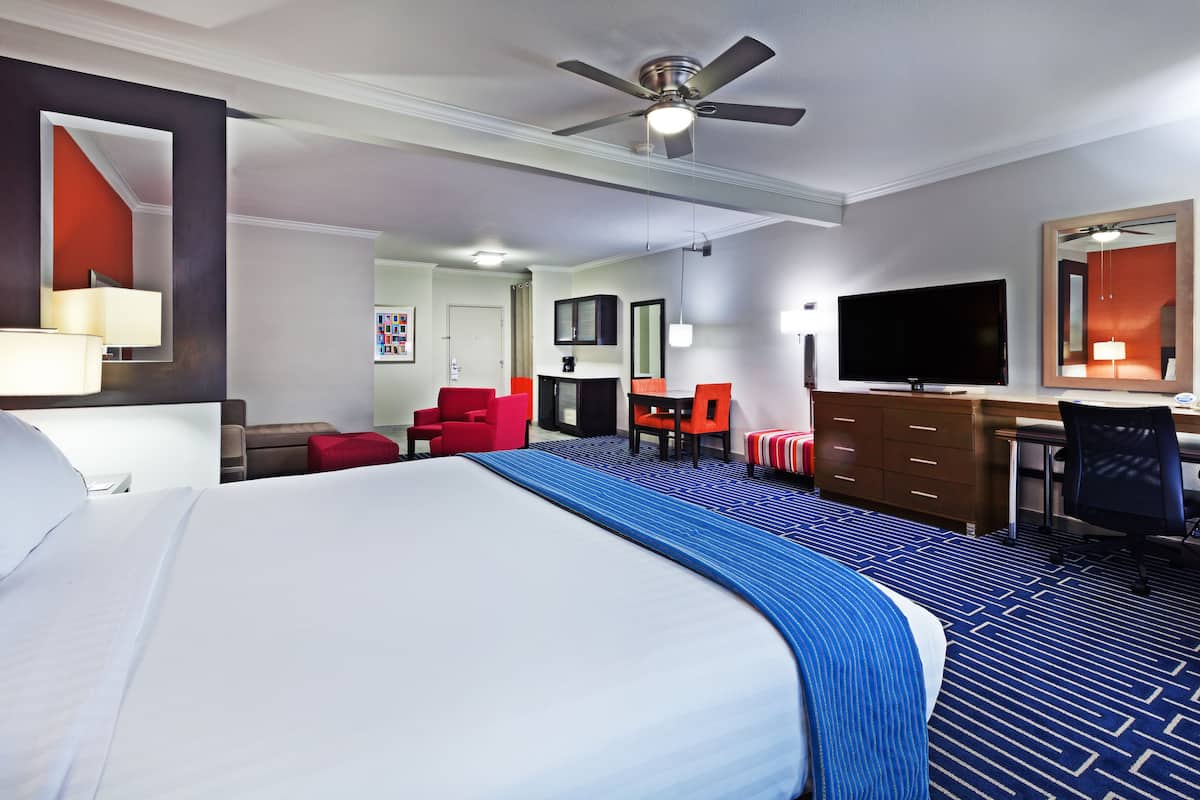 A hotel room with a large bed, a desk, a chair, a television, and a ceiling fan.
