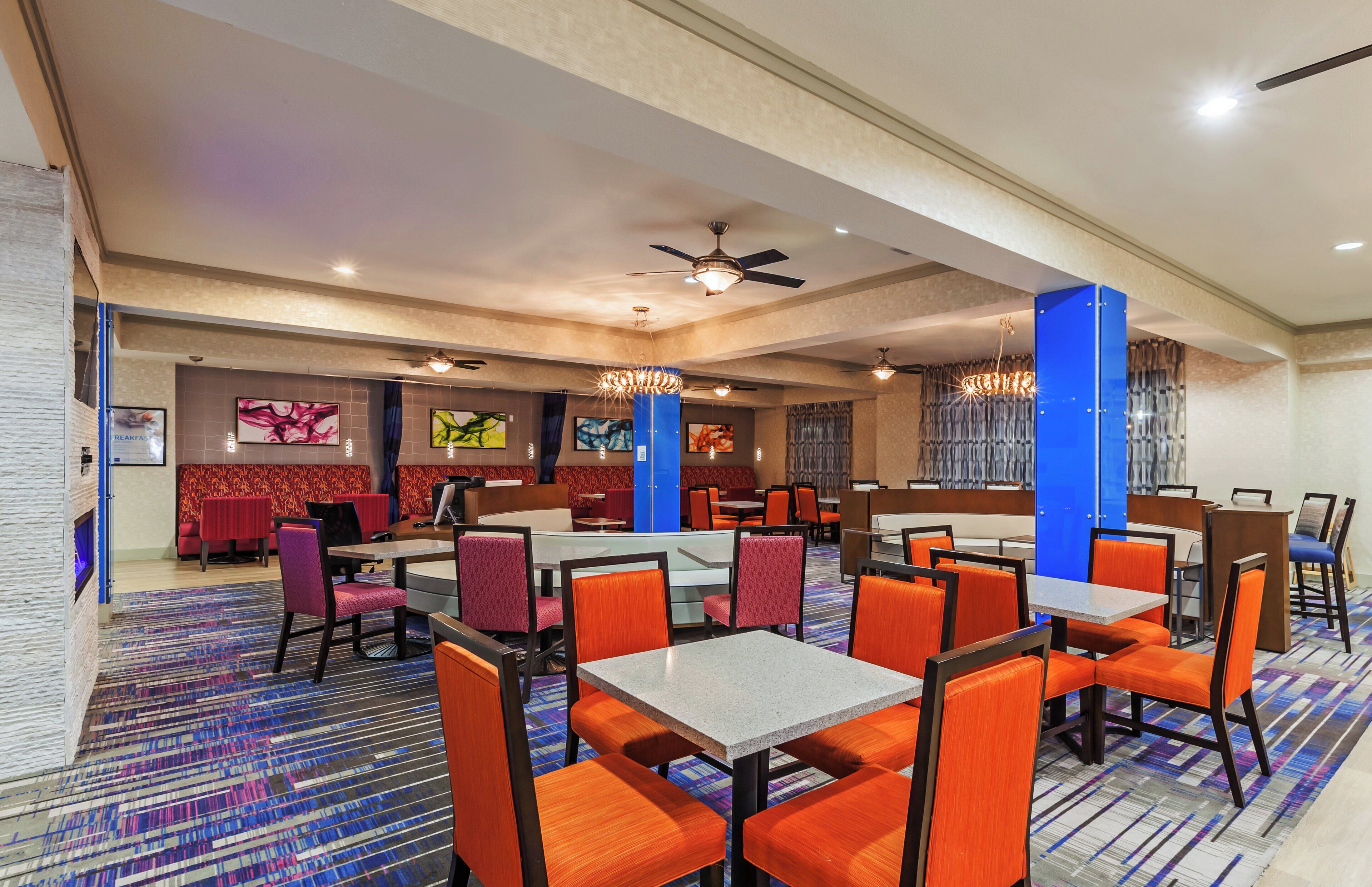 A hotel dining area with multiple tables and chairs, ceiling fans, and artwork on the walls.