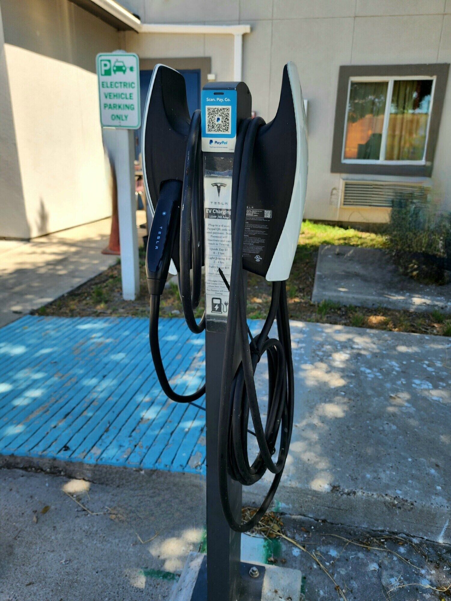 An electric vehicle charging station with a QR code and PayPal logo, a Tesla logo, and a sign indicating it is for electric vehicles only.