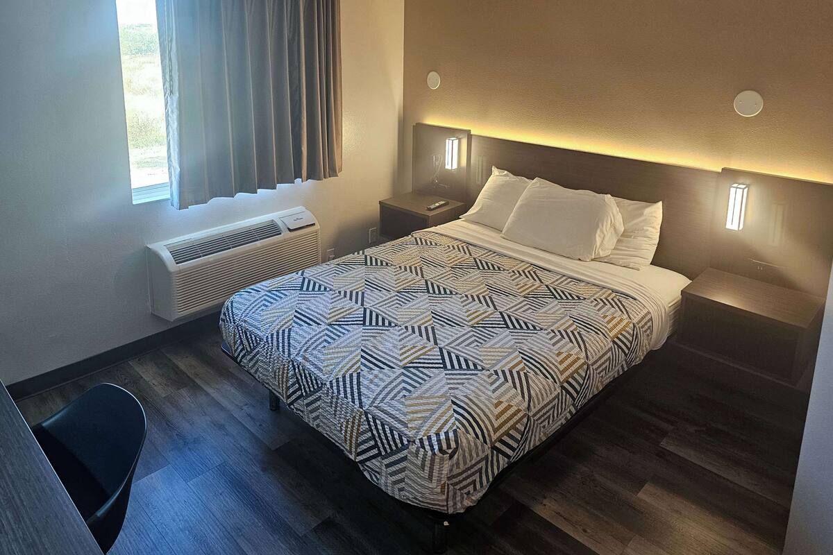 A hotel room with a bed, bedside tables, a desk, and a chair.