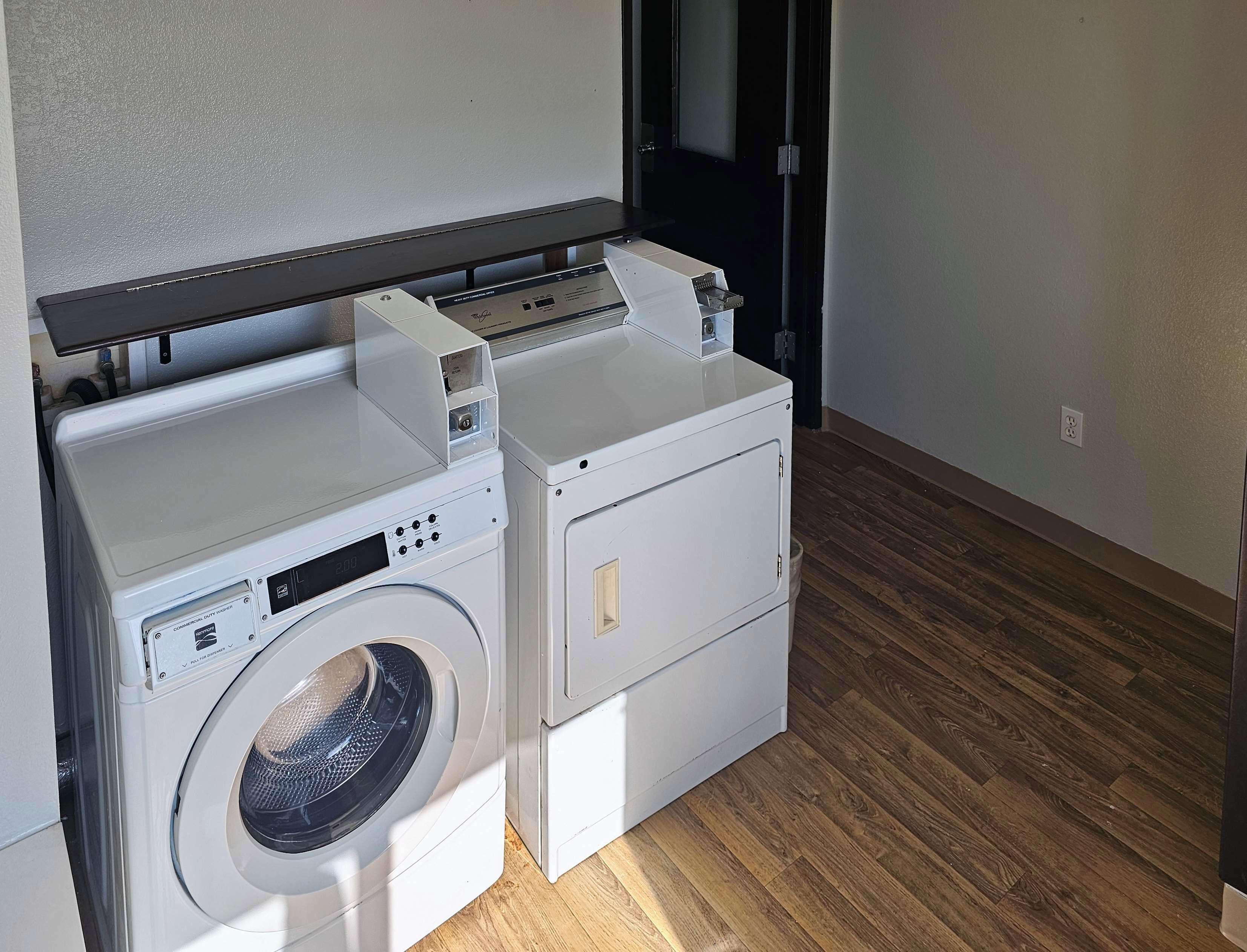 A compact laundry area with a front-loading washer and dryer, wooden flooring, and a door leading to another room.
