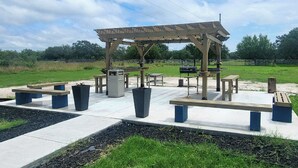 Un espace extérieur aménagé en terrasse, avec des tables de pique-nique, des bancs et une structure en forme de pergola.