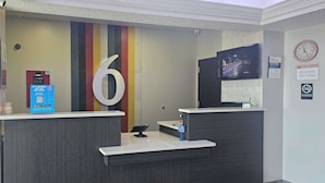 Un comptoir d’accueil avec un grand chiffre « 6 » affiché sur le mur, une horloge et un panneau « Il est interdit de fumer ».