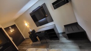 Un salon moderne avec un téléviseur à écran plat fixé au mur, un bureau en bois foncé, une chaise et une petite table avec une lampe.