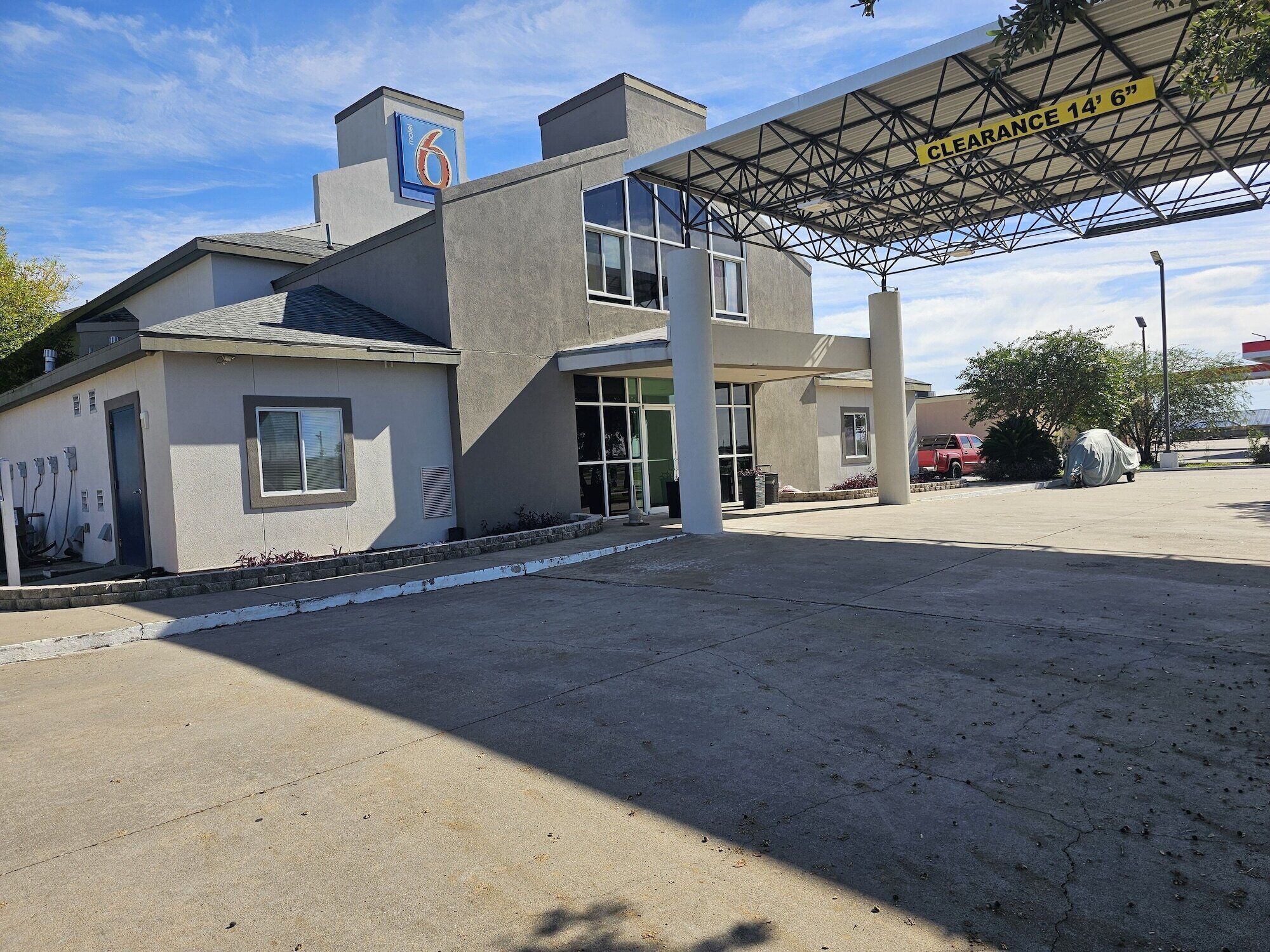 A motel with a covered parking area, a clear sky, and a red car parked outside.